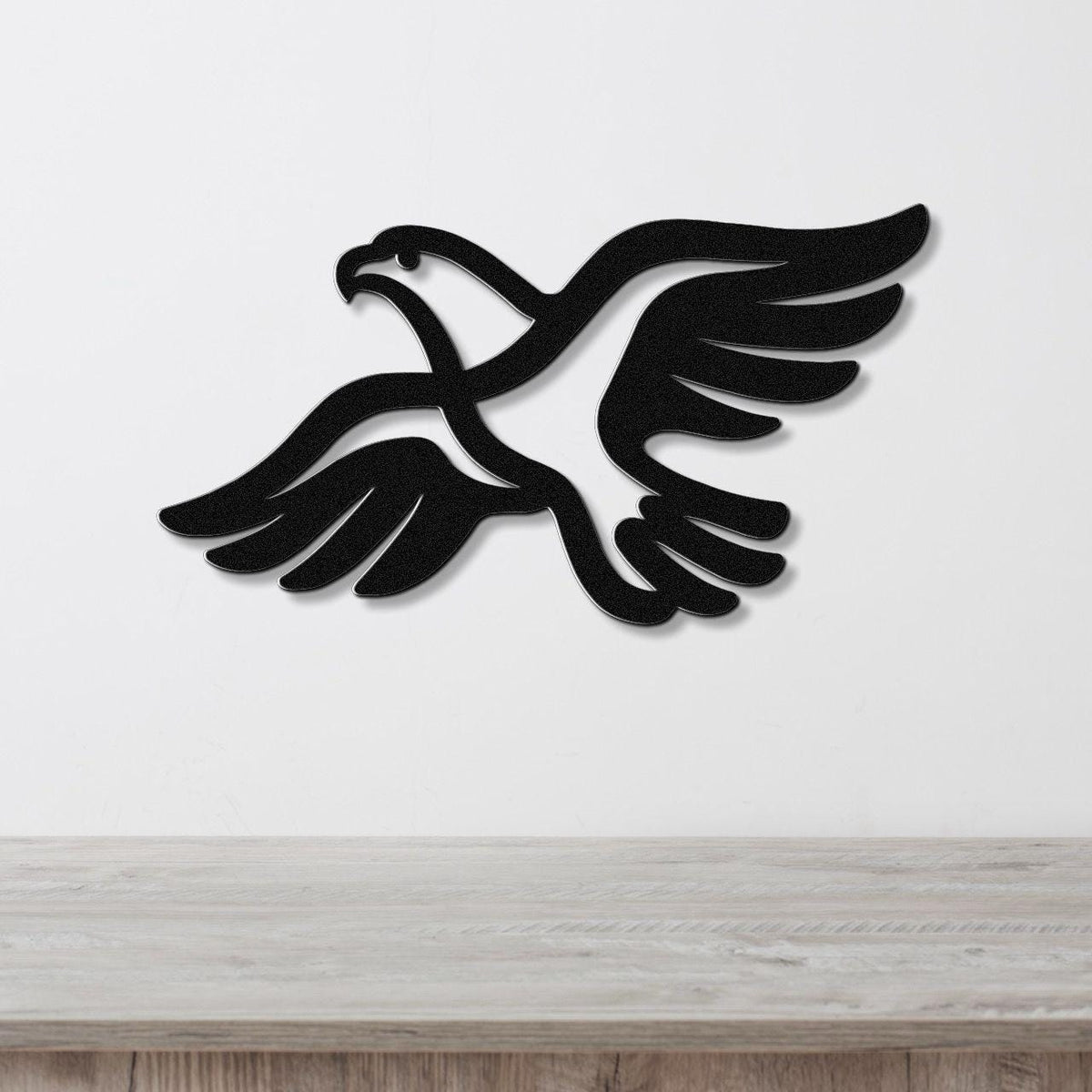 Black metal eagle wall art with outstretched wings and internal cutout details, mounted on a white wall above a light wood countertop.