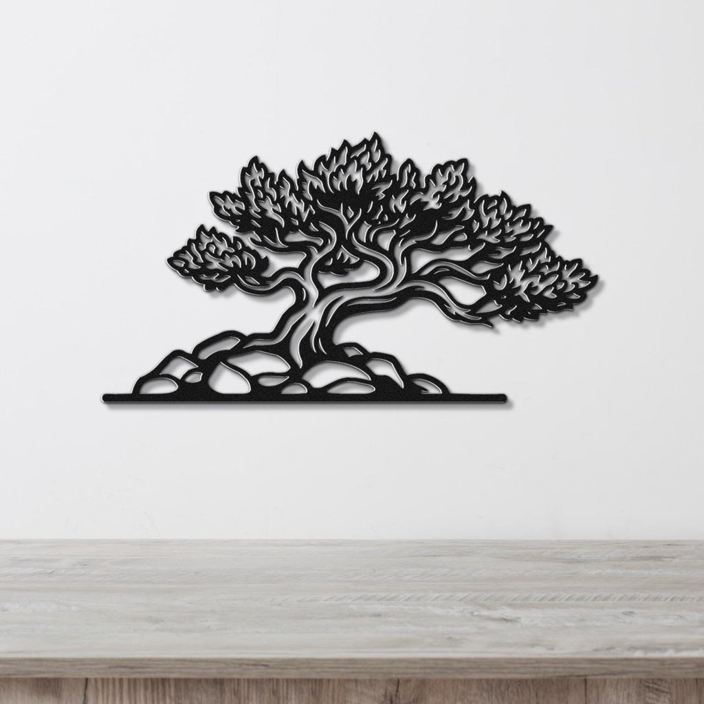 Black metal wall art cutout of a juniper tree with detailed branches and foliage, mounted on a white wall above a wooden surface.
