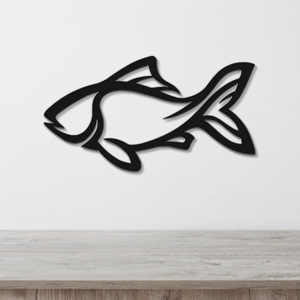 Black metal fish wall art with internal cutout details, mounted on a white wall above a light wood surface.