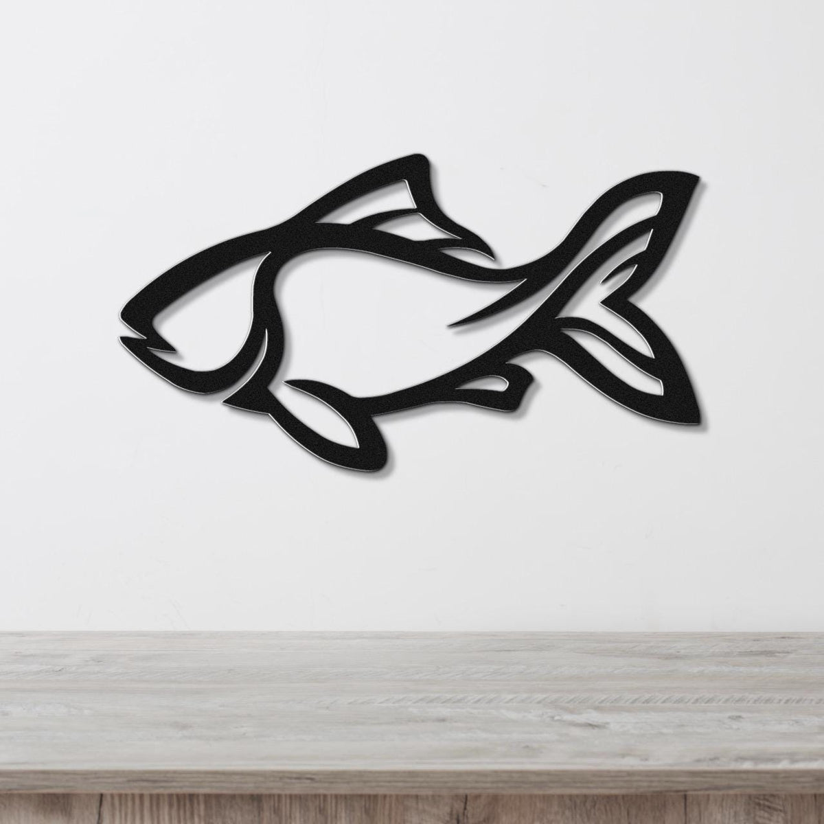 Black metal fish wall art with internal cutout details, mounted on a white wall above a light wood surface.