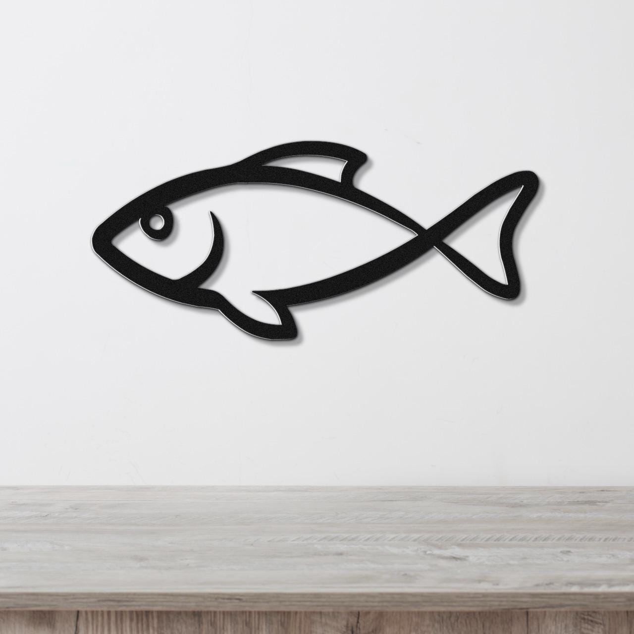Black metal fish wall art with a silhouette cutout design, mounted on a white wall above a light wood countertop.