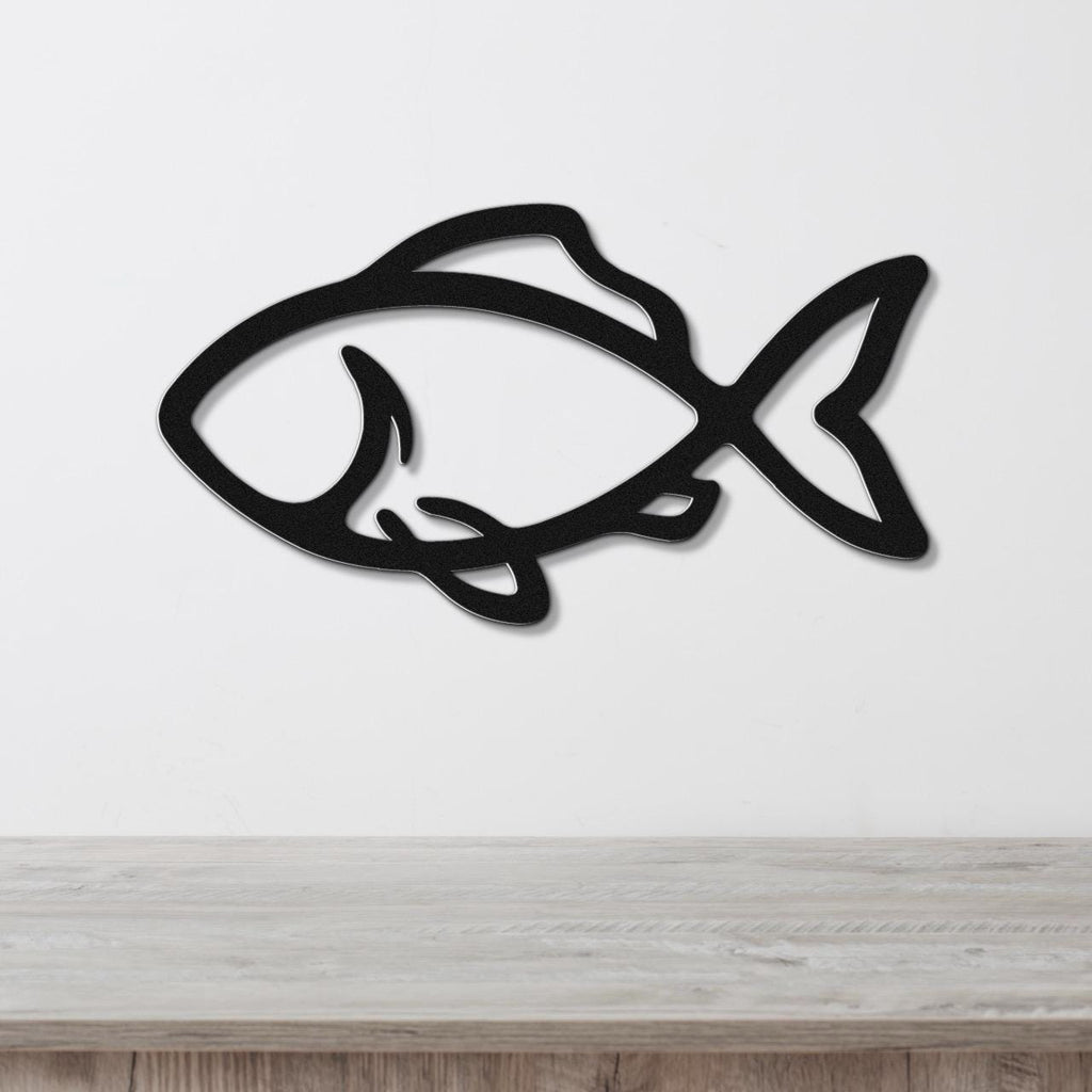 Black metal fish wall art with bold silhouette and internal cutout details, mounted on a white wall above a light wood countertop.