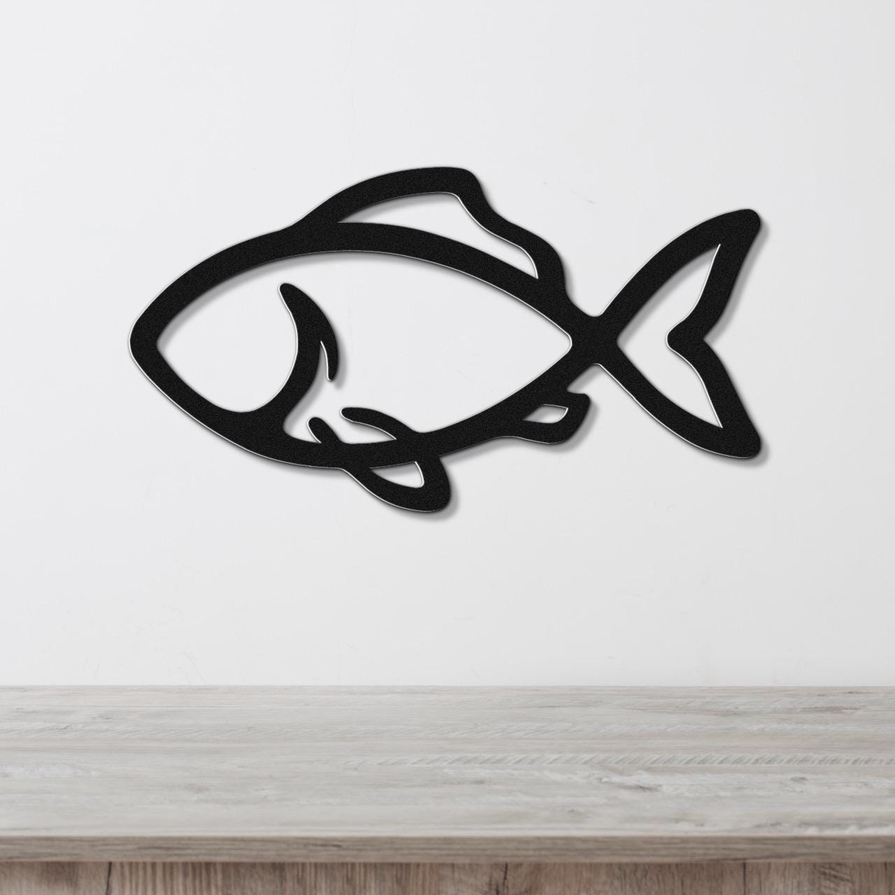 Black metal fish wall art with bold silhouette and internal cutout details, mounted on a white wall above a light wood countertop.