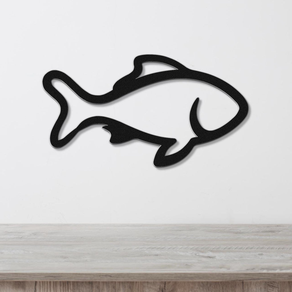 Black metal fish wall art with bold outline and internal cutouts, mounted on a white wall above a light wood surface.