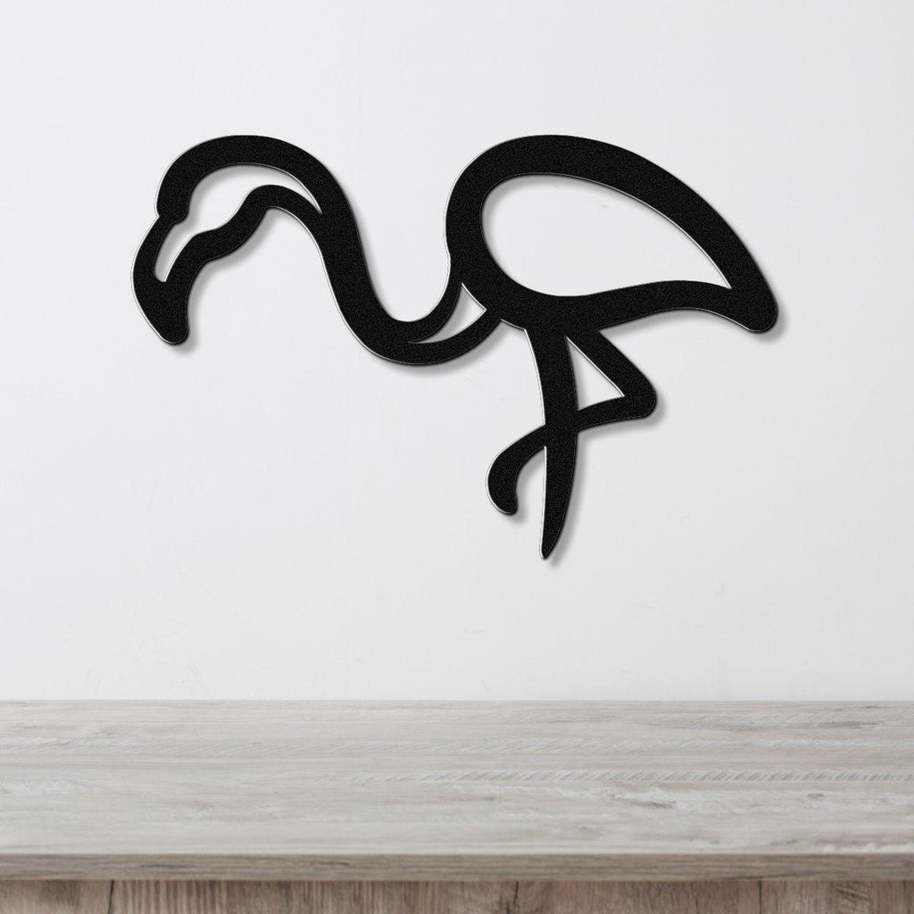 Black metal flamingo wall art with a bold silhouette design, mounted on a white wall above a light wood surface.