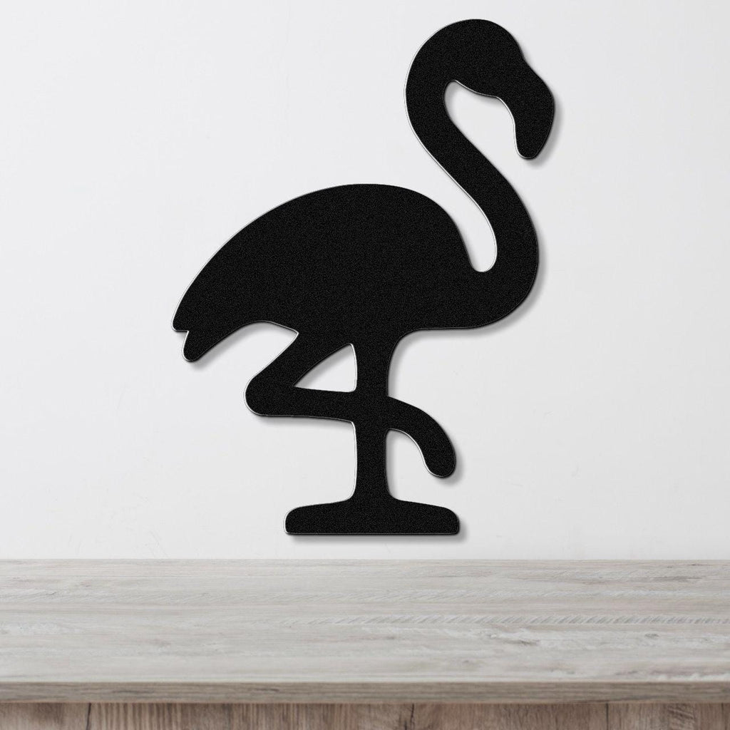 Black metal flamingo wall art silhouette with cutout details, mounted on a white wall above a light wood surface.