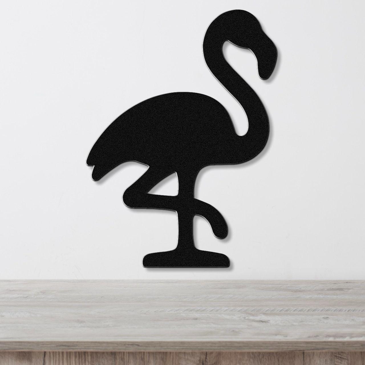 Black metal flamingo wall art silhouette with cutout details, mounted on a white wall above a light wood surface.