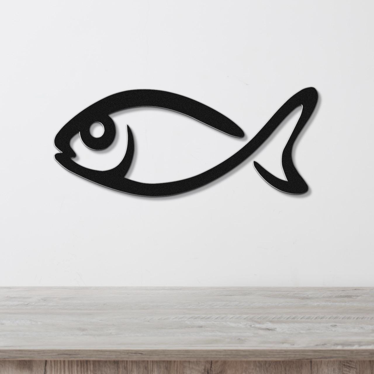 Black metal fish wall art with a bold silhouette design, mounted on a white wall above a light wood surface.
