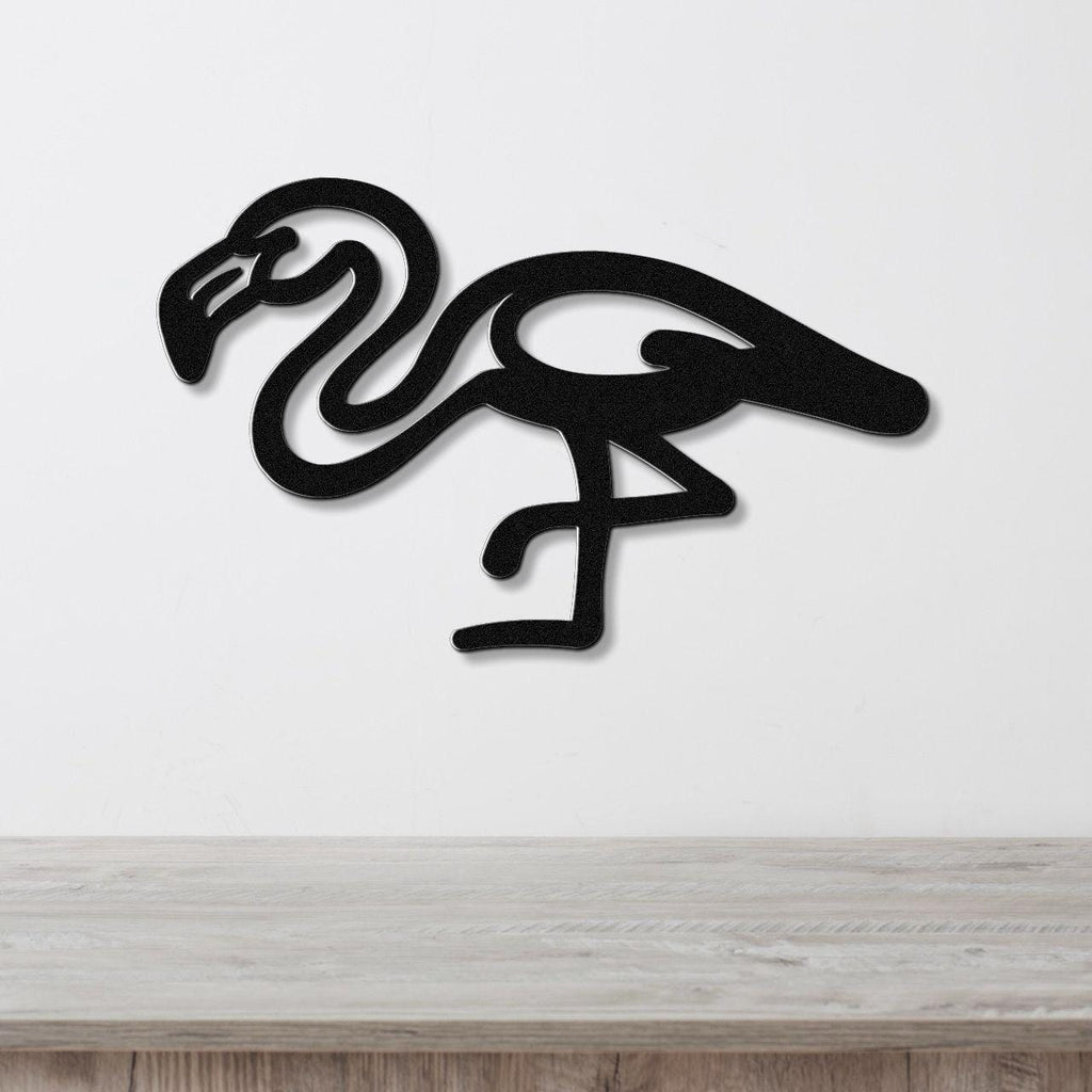 Black metal flamingo wall art with a minimalist silhouette design, mounted on a white wall above a light wood surface.