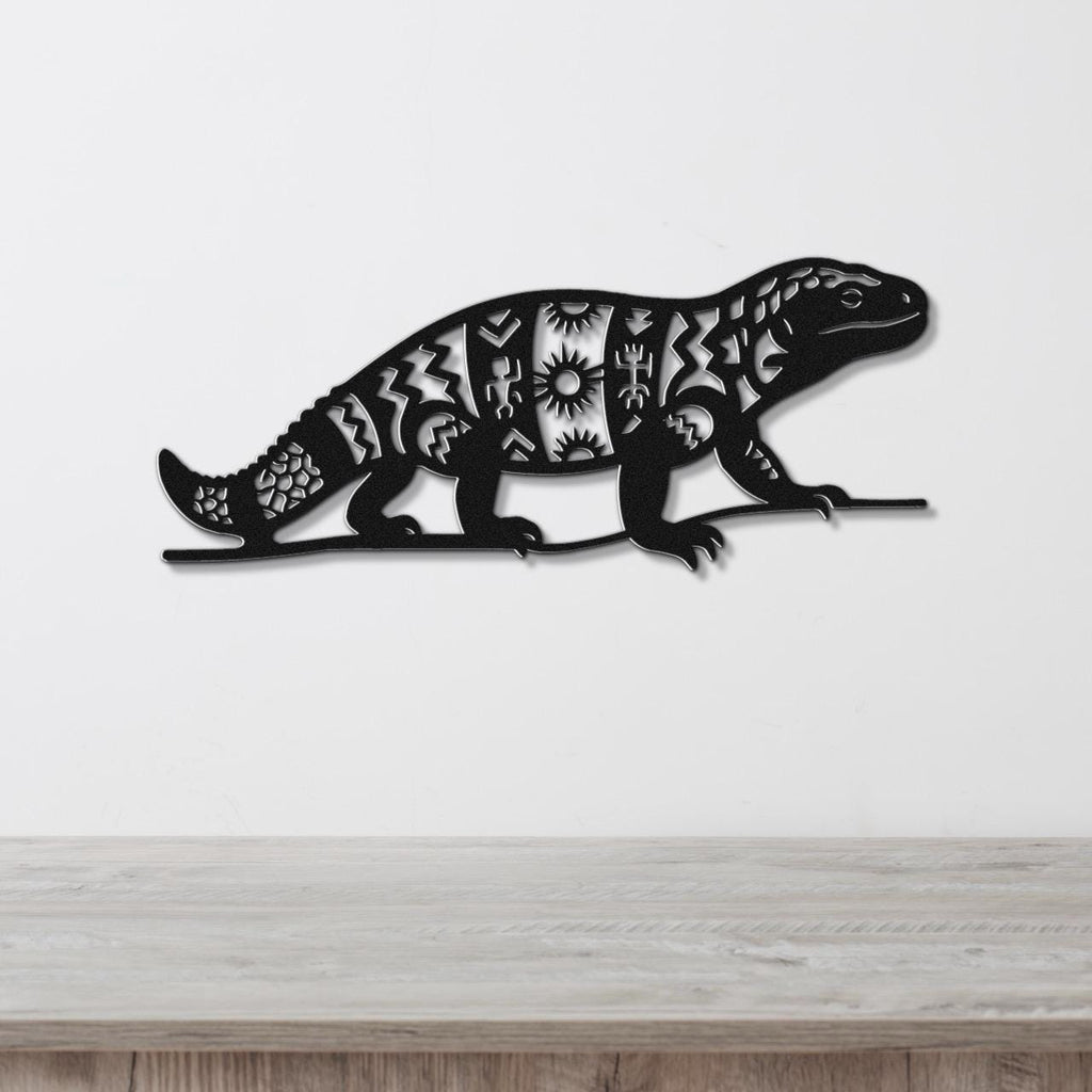 Black metal wall art of a Gila monster with intricate geometric and sunburst cutouts, mounted on a white wall above a wooden surface.