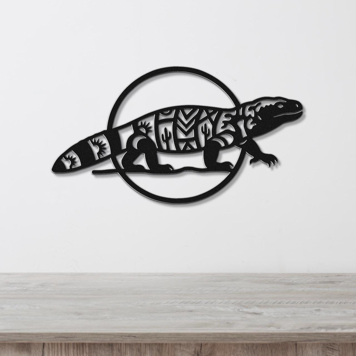 Black metal Gila monster wall art with intricate cutout patterns, mounted on a white wall above a wooden surface.