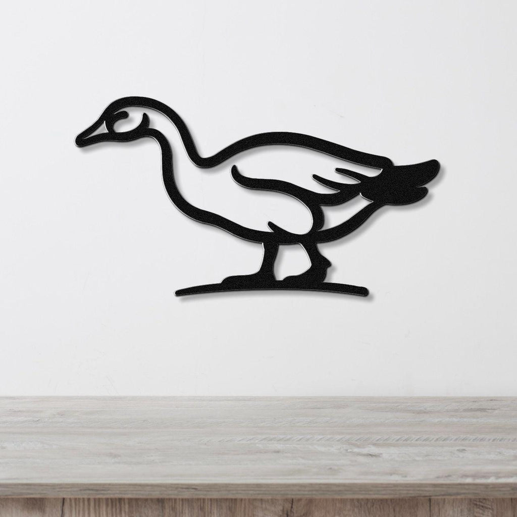 Black metal goose wall art silhouette with internal cutout details, mounted on a white wall above a light wood surface.
