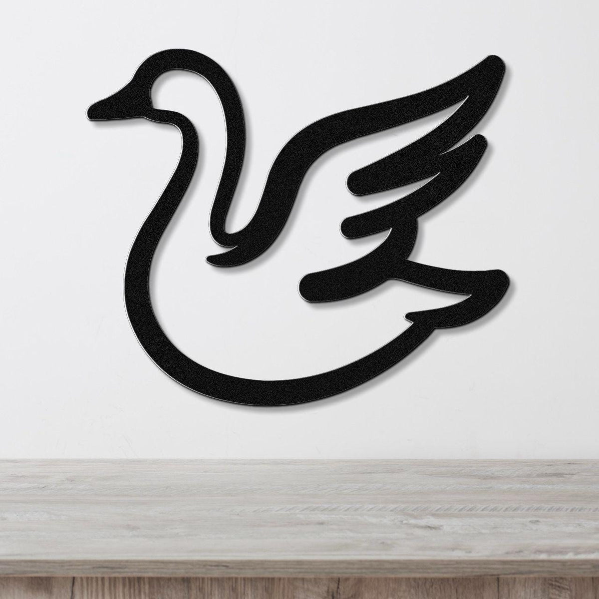 Black metal goose wall art silhouette with layered wing cutouts, mounted on a white wall above a light wood surface.