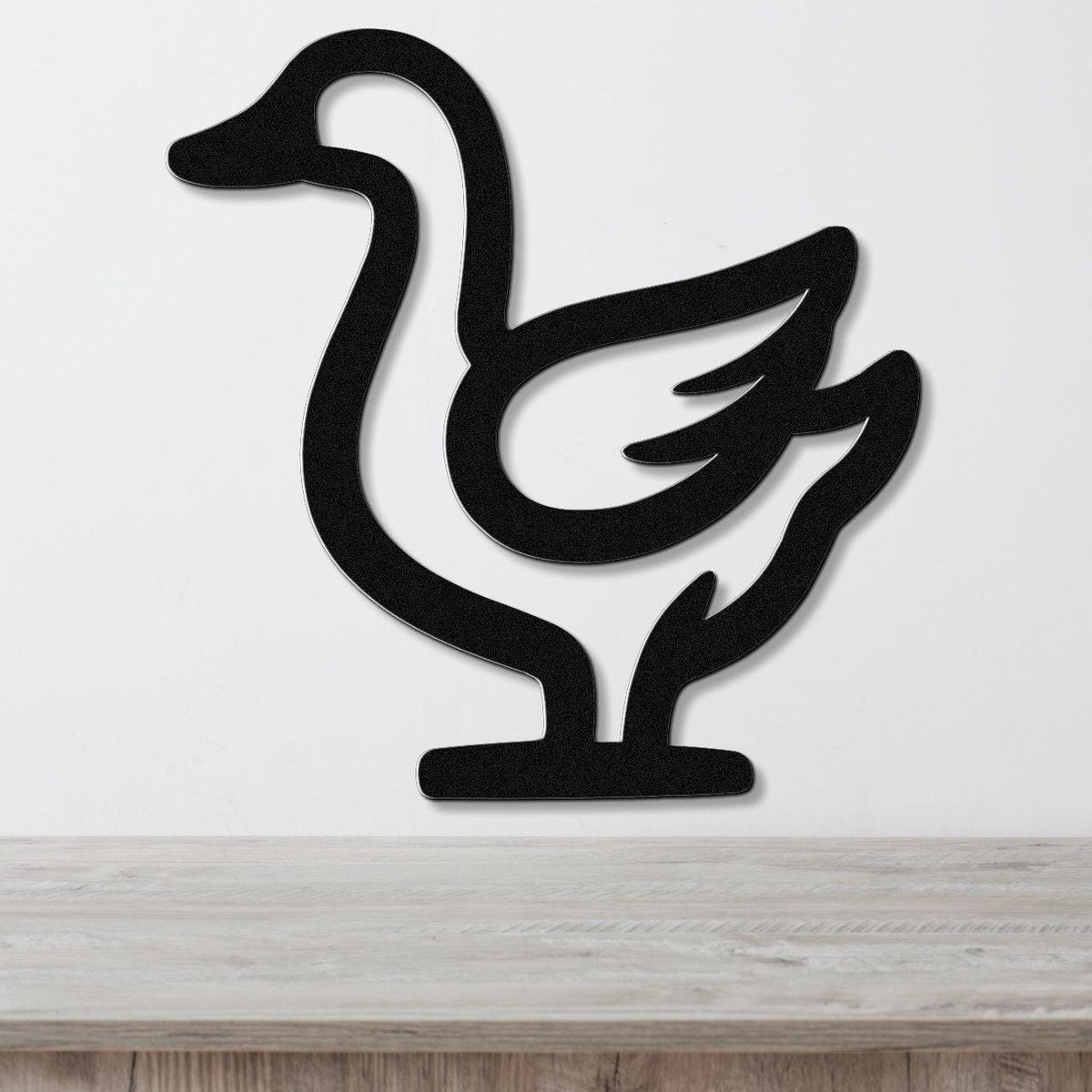Black metal goose wall art silhouette with cutout wing and neck details, mounted on a white wall above a light wood surface.