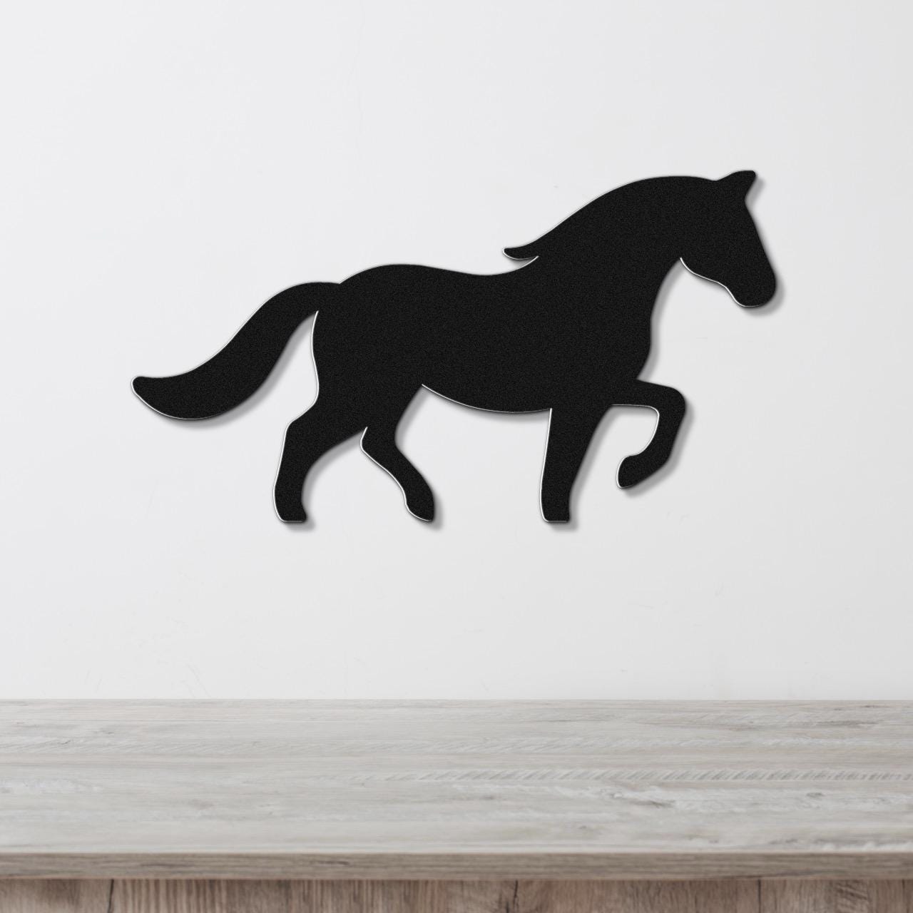 Black metal horse silhouette wall art with a dynamic running pose, mounted on a white wall above a light wood surface.