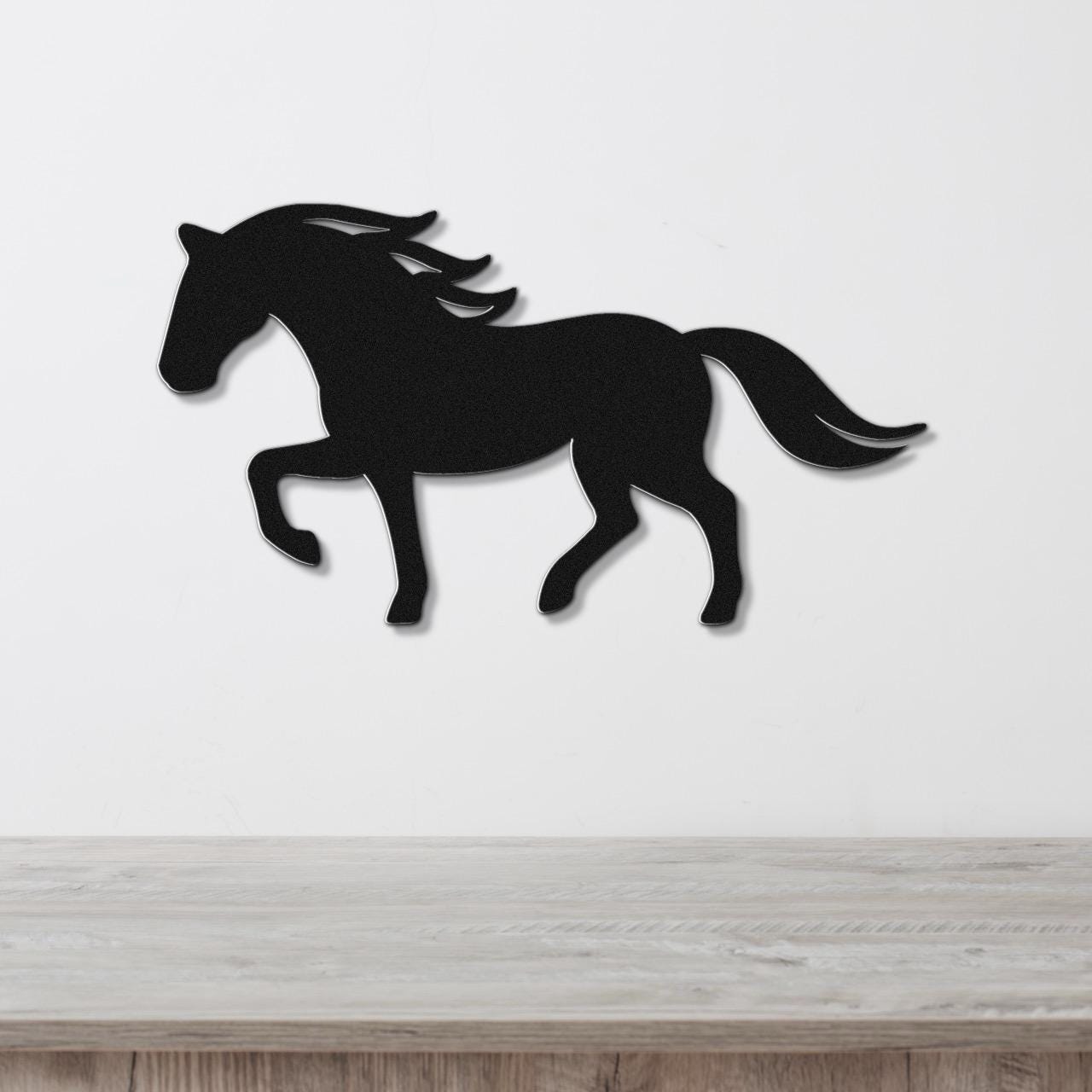 Black metal horse wall art silhouette with flowing mane and tail cutouts, mounted on a white wall above a light wood surface.