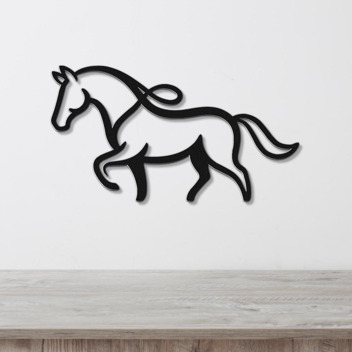 Black metal horse wall art with flowing mane and tail cutouts, mounted on a white wall above a light wood surface.