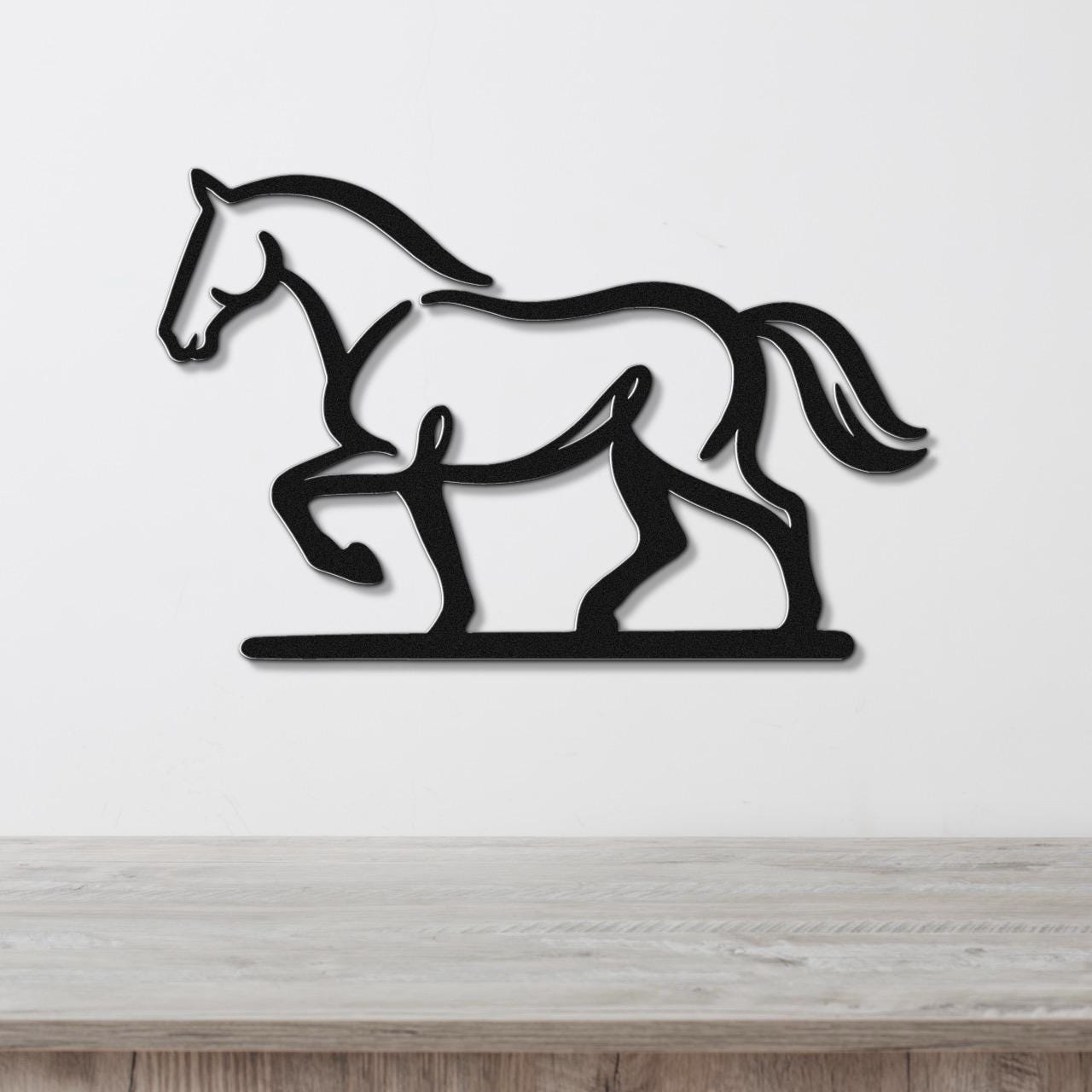 Black metal horse wall art in a silhouette style, mounted on a white wall above a light wood surface.