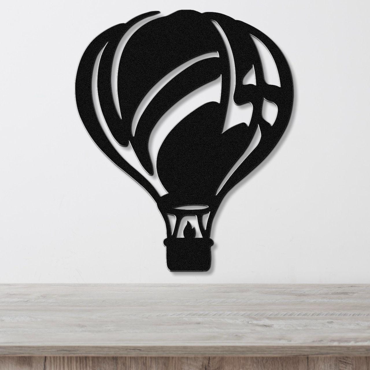 Black metal wall art in the silhouette of a hot air balloon with internal cutout details, mounted on a white wall above a light wood surface.
