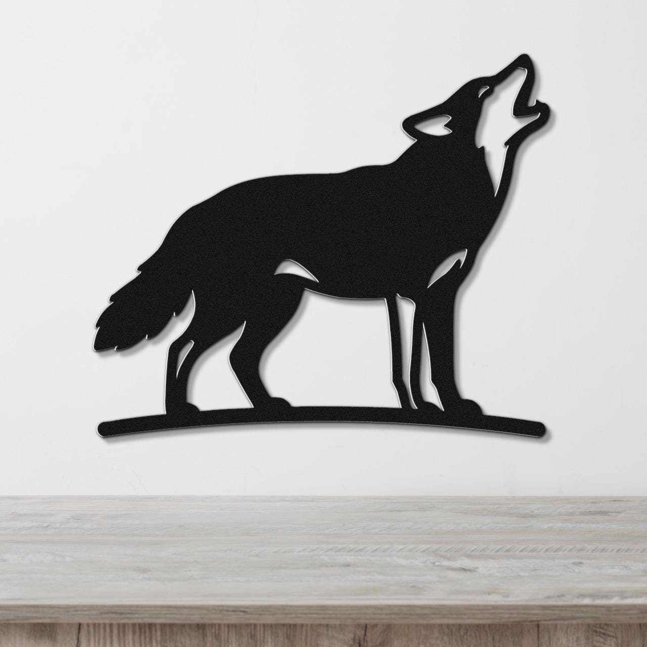Black metal coyote wall art in a howling silhouette, mounted on a white wall above a light wood counter.
