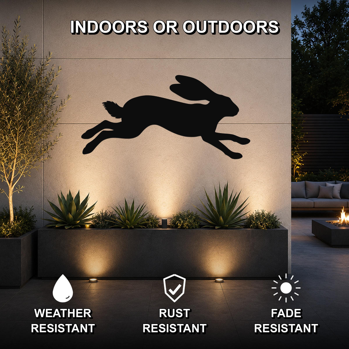 Black metal jackrabbit wall art silhouette mounted on an outdoor wall above a planter, illuminated by uplights in a patio setting.