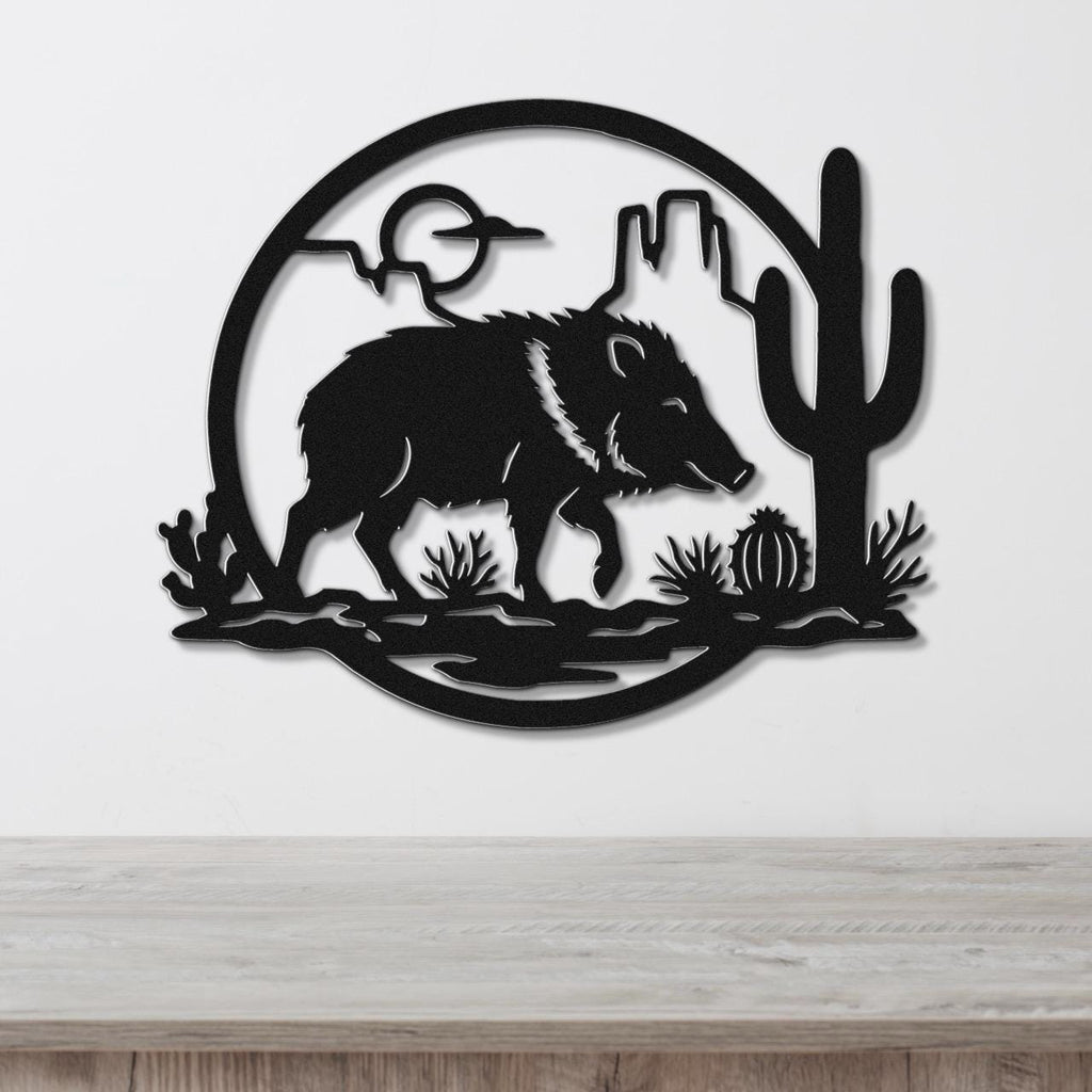 Black metal wall art silhouette of a javelina in a desert scene with cactus and mountains, mounted on a white wall above a wooden surface.