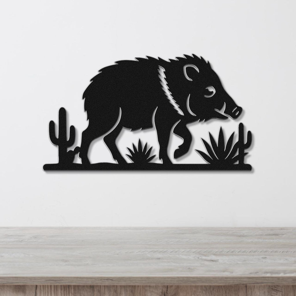 Black metal wall art cutout of a javelina with cacti and agave plants, mounted on a white wall above a wooden surface.