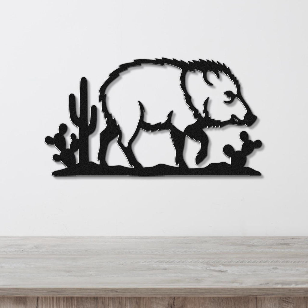 Black metal wall art silhouette of a javelina with cacti, mounted on a white wall above a wooden surface.