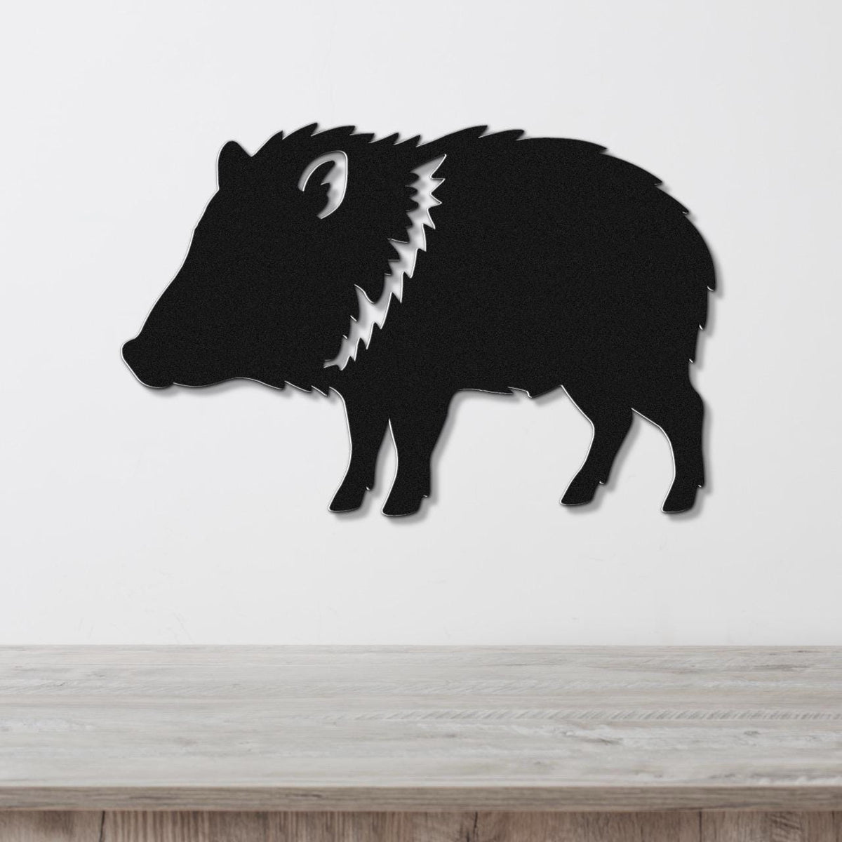 Black metal javelina wall art silhouette with a white zigzag cutout along the neck, mounted on a white wall above a light wood surface.