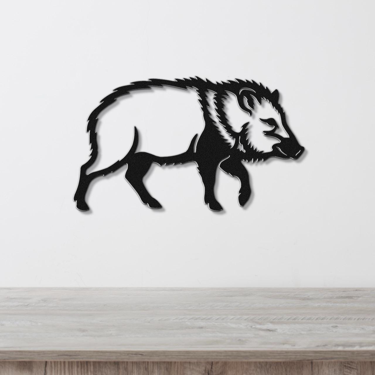 Black metal javelina wall art silhouette with detailed fur and facial features, mounted on a white wall above a light wood surface.