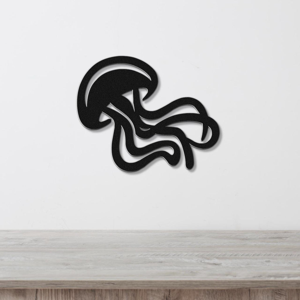Black metal jellyfish wall art with flowing tentacle cutouts, mounted on a white wall above a light wood surface.