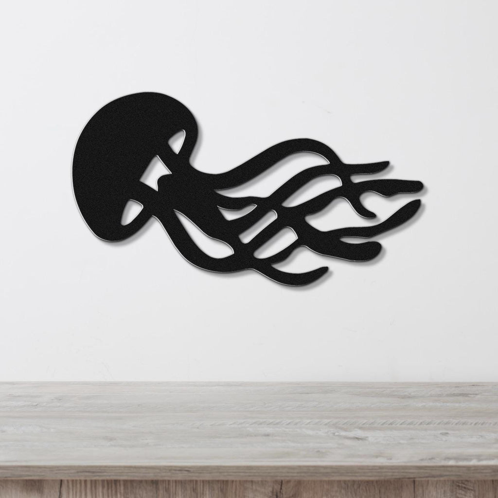 Black metal jellyfish wall art with flowing tentacle cutouts, mounted on a white wall above a light wood surface.
