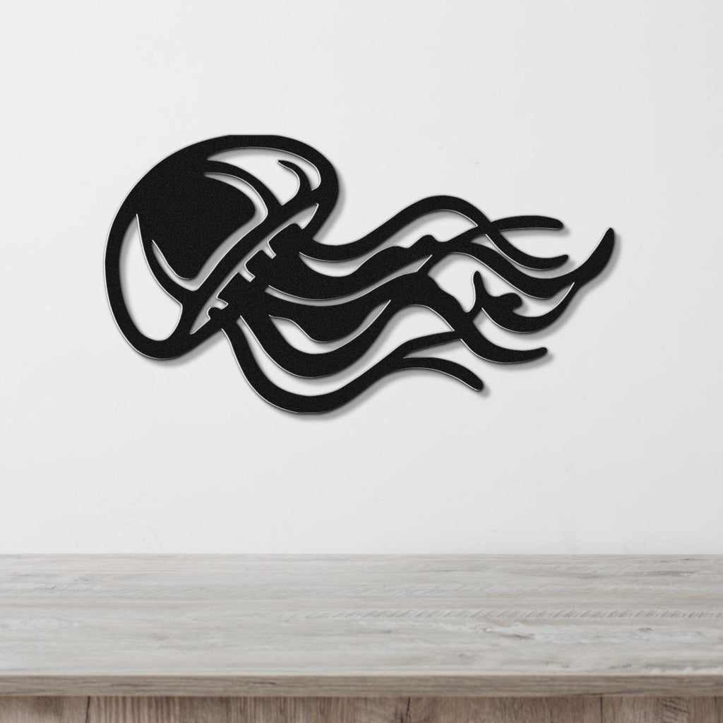 Black metal jellyfish wall art with flowing tentacle cutouts, mounted on a white wall above a light wood surface.
