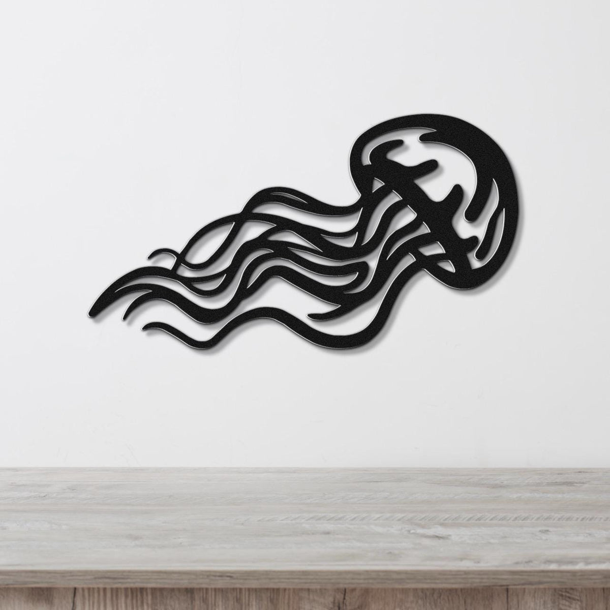 Black metal jellyfish wall art with flowing tentacle cutouts, mounted on a white wall above a light wood counter.