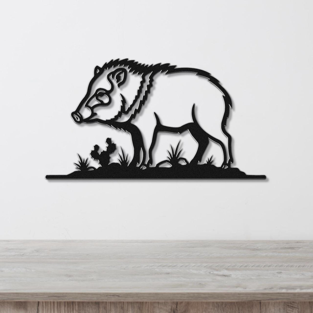 Black metal wall art silhouette of a javelina with grass cutouts, mounted on a white wall above a wooden surface.