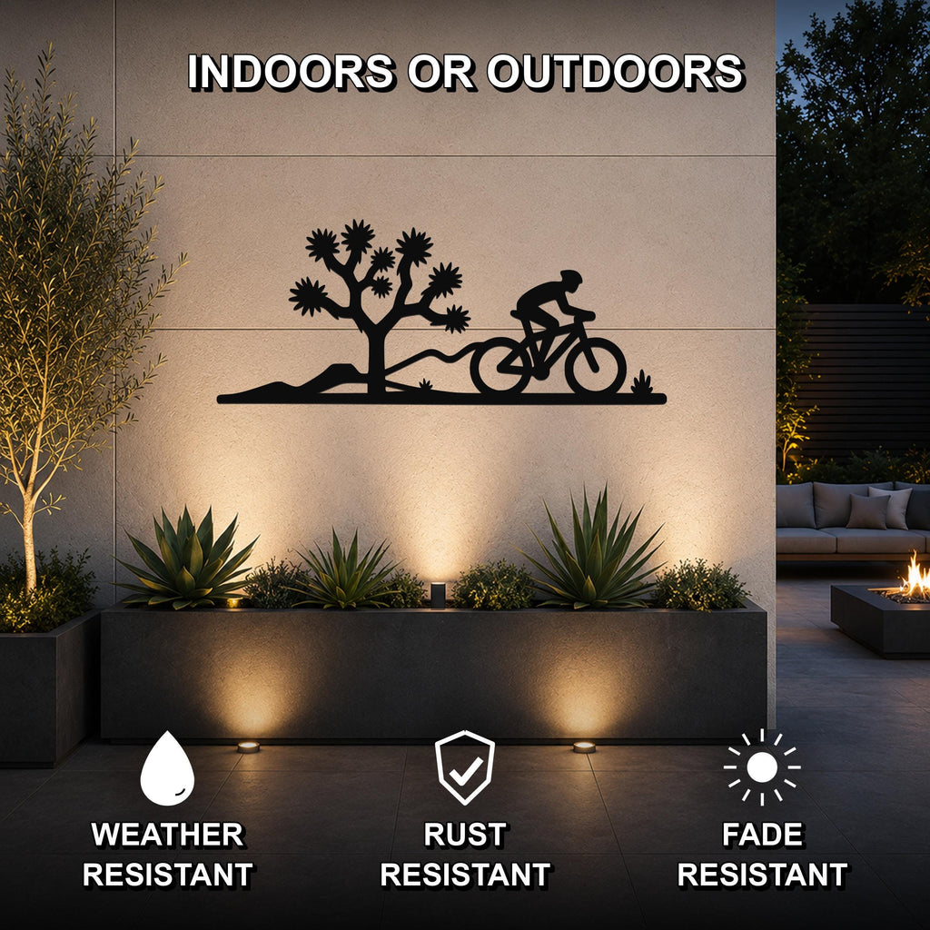Black metal wall art featuring a desert silhouette of a Joshua tree and a cyclist, mounted on an outdoor wall above a planter with succulents.