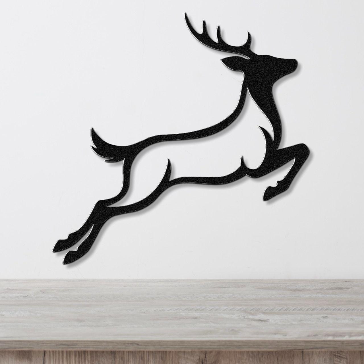 Black metal wall art of a leaping deer silhouette with antlers and motion lines, mounted on a white wall above a light wood surface.
