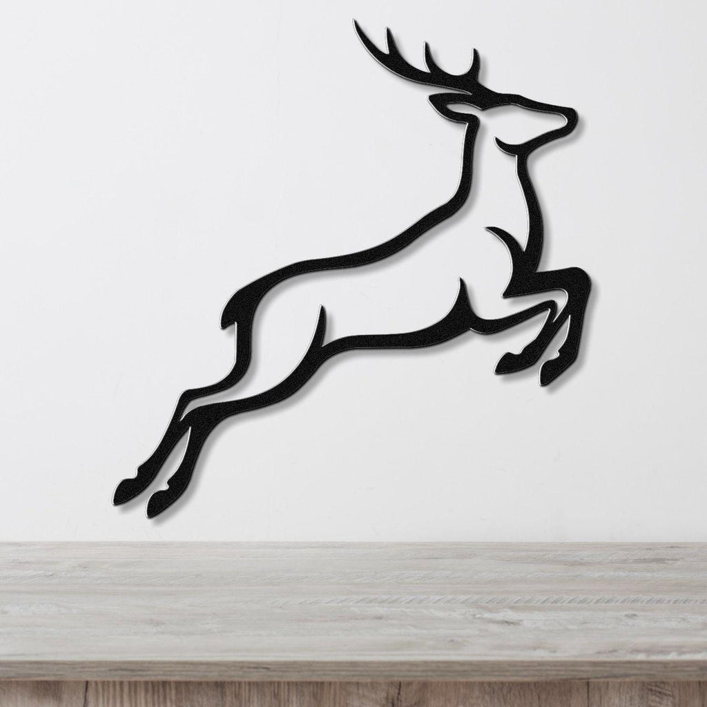 Black metal wall art of a leaping deer silhouette with antlers, mounted on a white wall above a light wood surface.