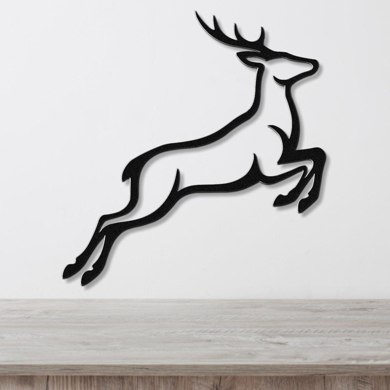 Black metal wall art of a leaping deer silhouette with antlers, mounted on a white wall above a light wood surface.