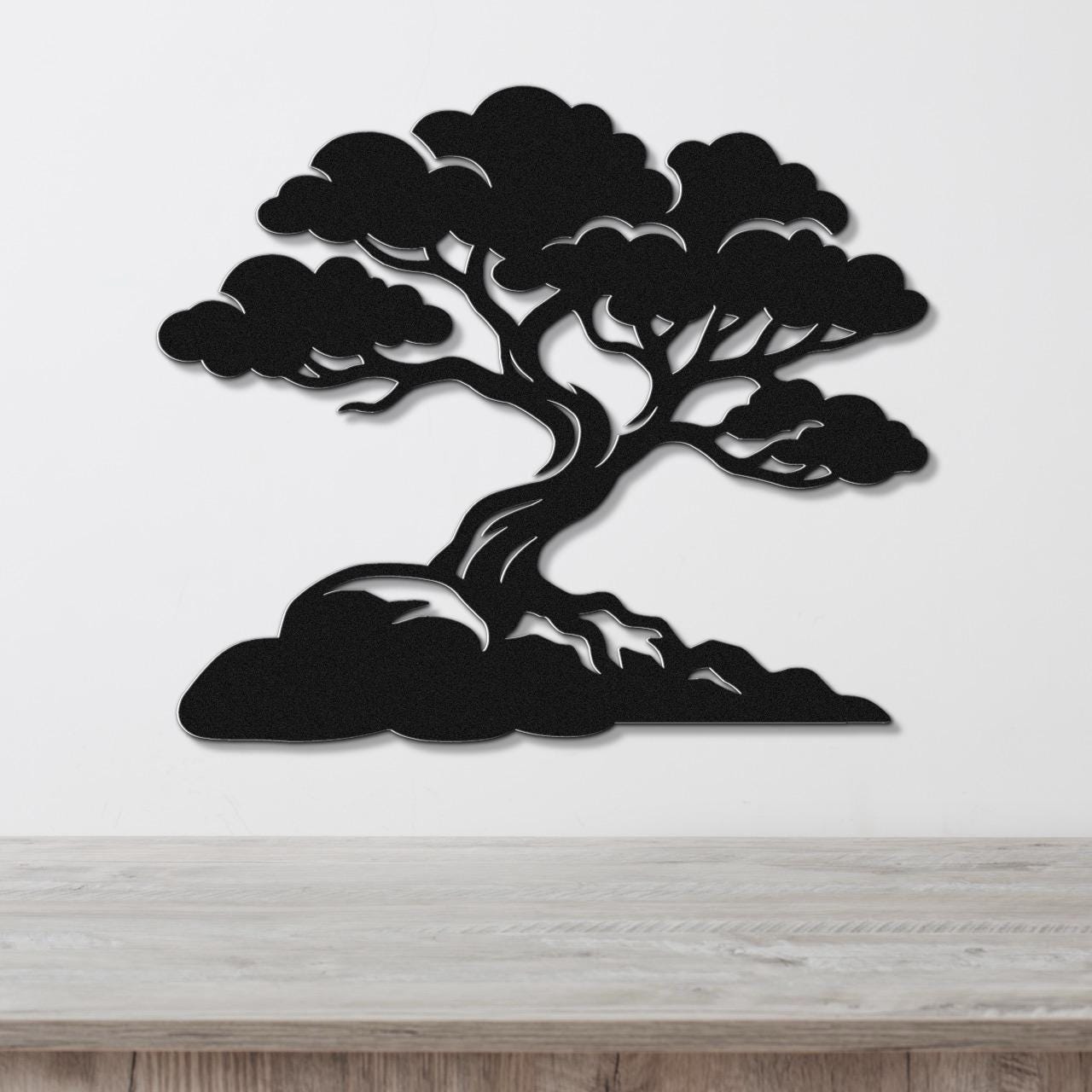 Black metal wall art cutout of a juniper tree with detailed branches and roots, mounted on a white wall above a wooden surface.