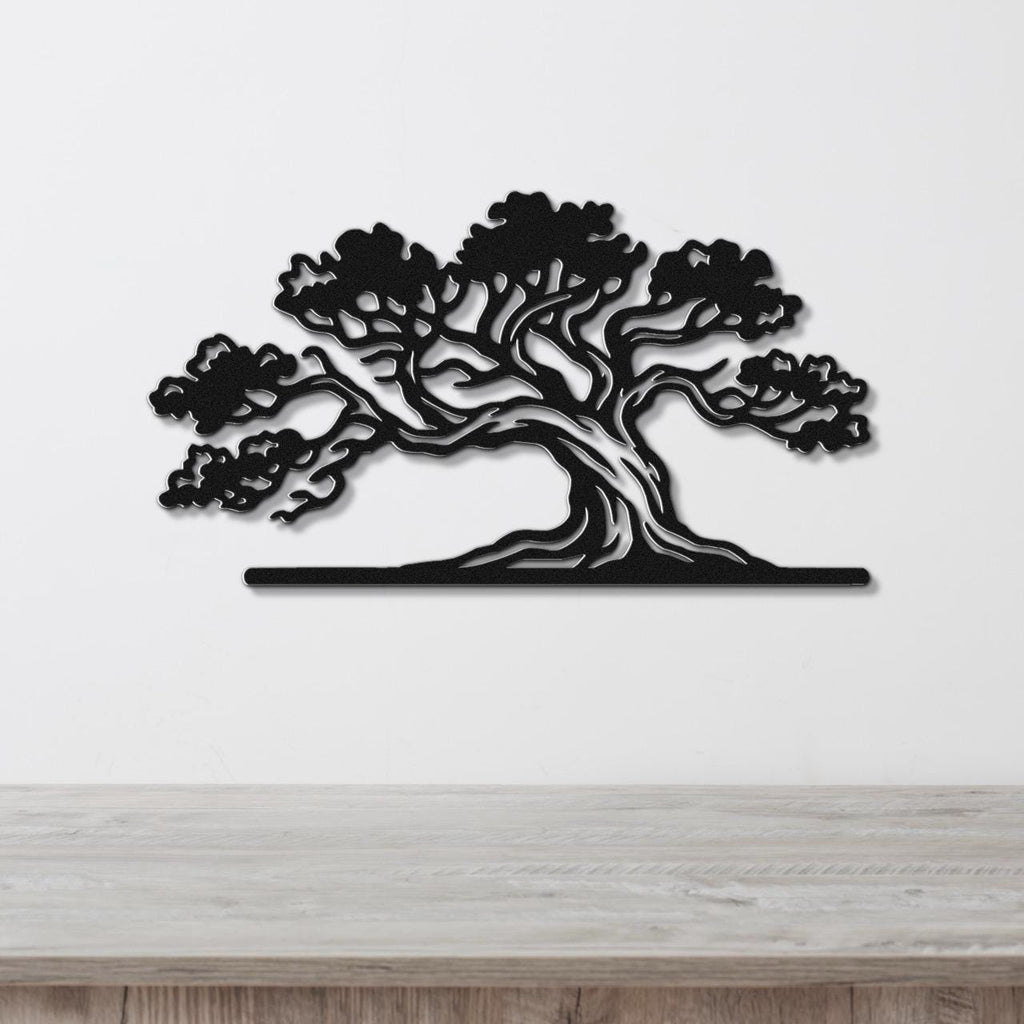 Black metal juniper tree wall art with intricate branch and foliage cutouts, mounted on a white wall above a wooden surface.