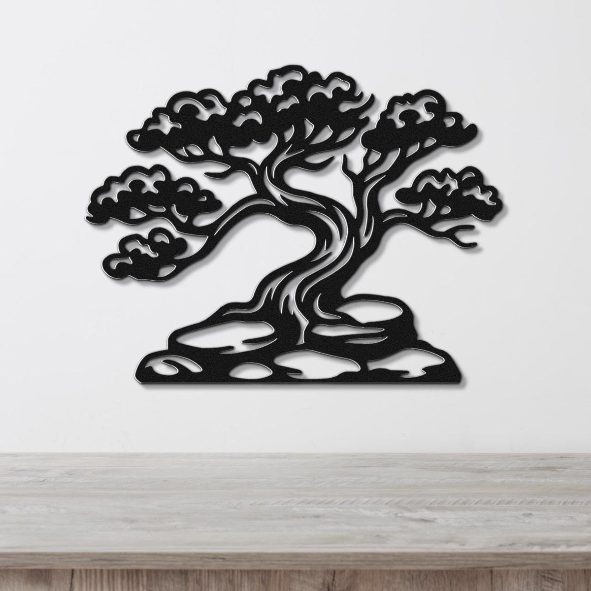 Black metal wall art cutout of a juniper tree with detailed branches and foliage, mounted on a white wall above a wooden surface.