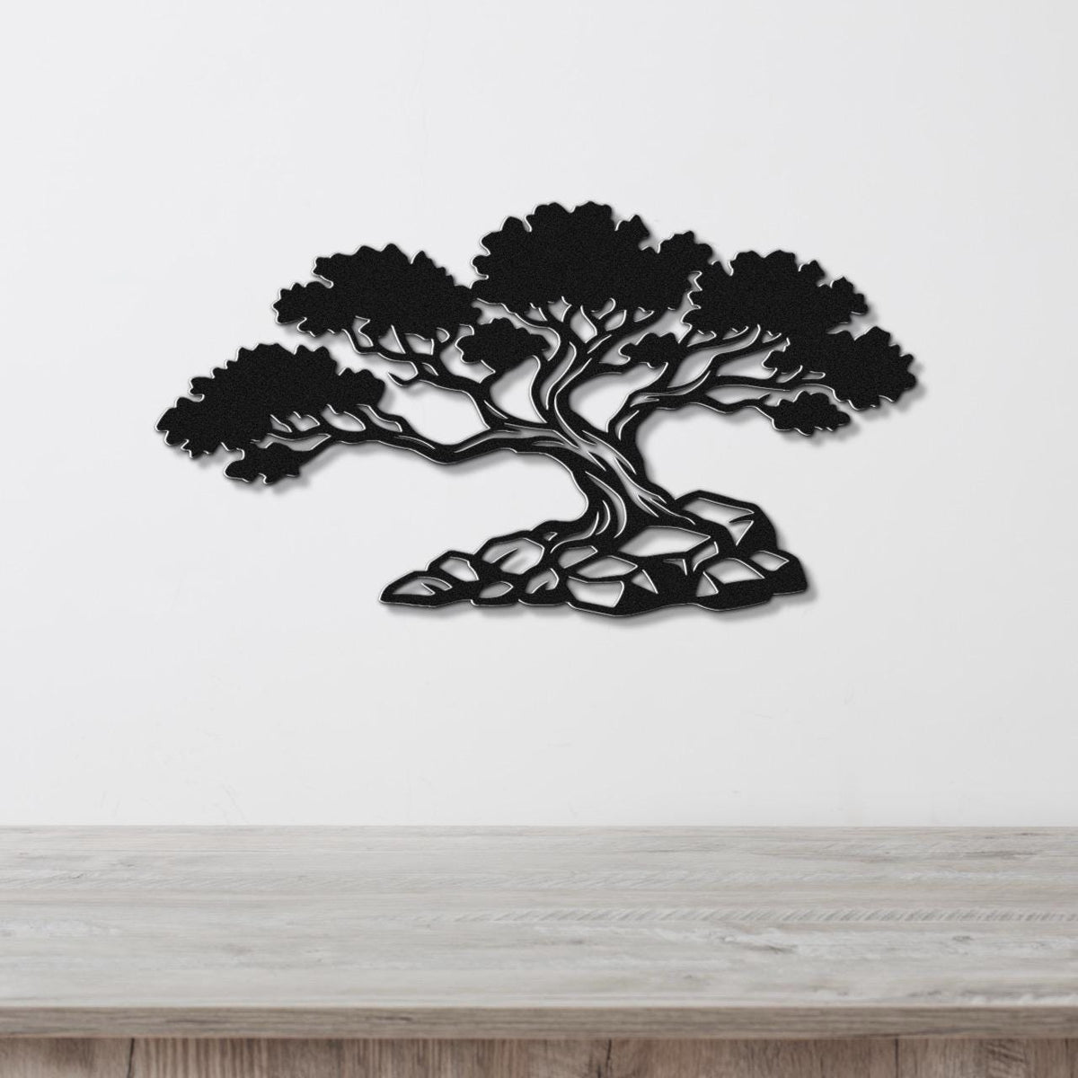 Black metal wall art cutout of a juniper tree with detailed branches and roots, mounted on a white wall above a wooden surface.