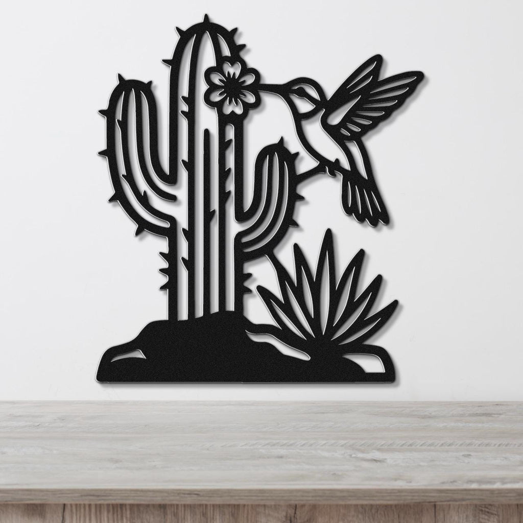 Black metal wall art featuring a cactus, hummingbird, and flower cutouts, mounted on a white wall above a wooden surface.