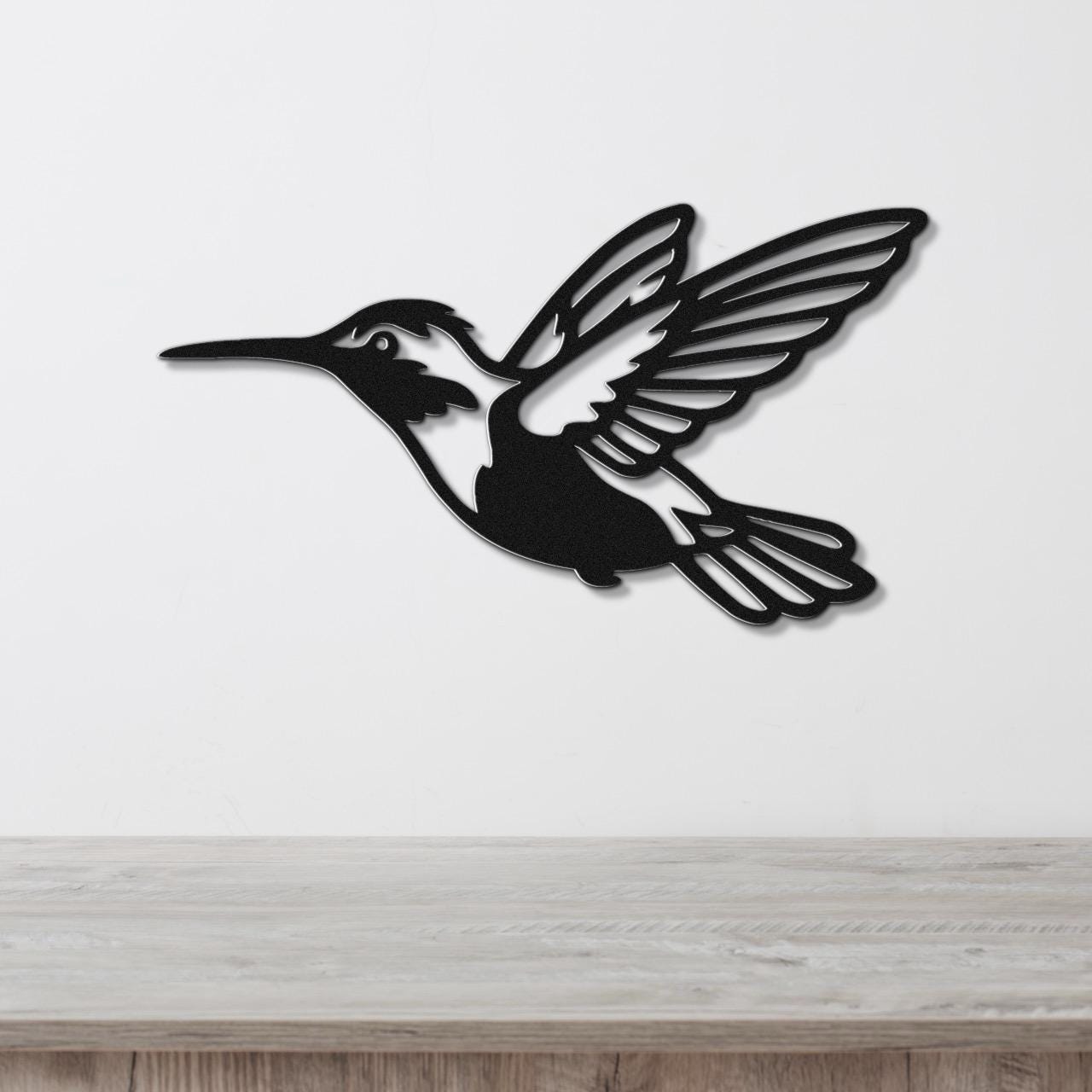 Black metal hummingbird wall art with cutout wings and tail, mounted on a white wall above a light wood counter.