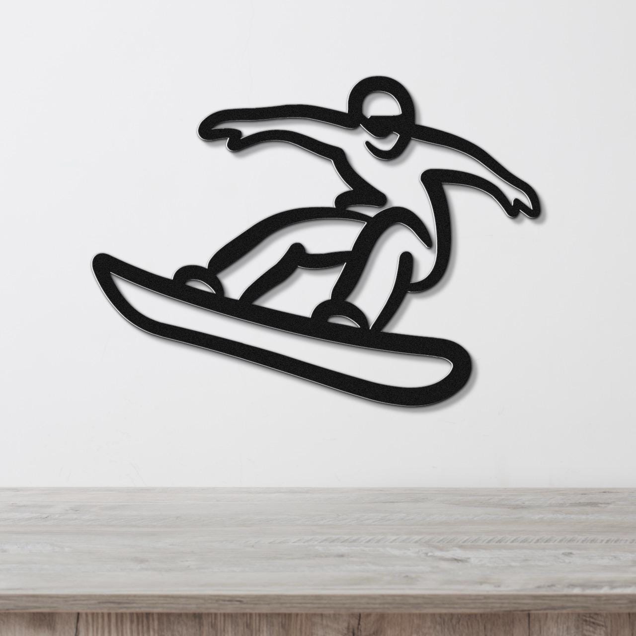 Black metal wall art cutout of a snowboarder in motion, mounted on a white wall above a light wood surface.