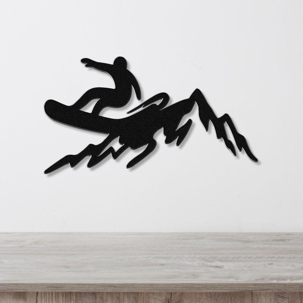 Black metal wall art silhouette of a snowboarder in mid-air above a mountain range, mounted on a white wall above a light wood counter.