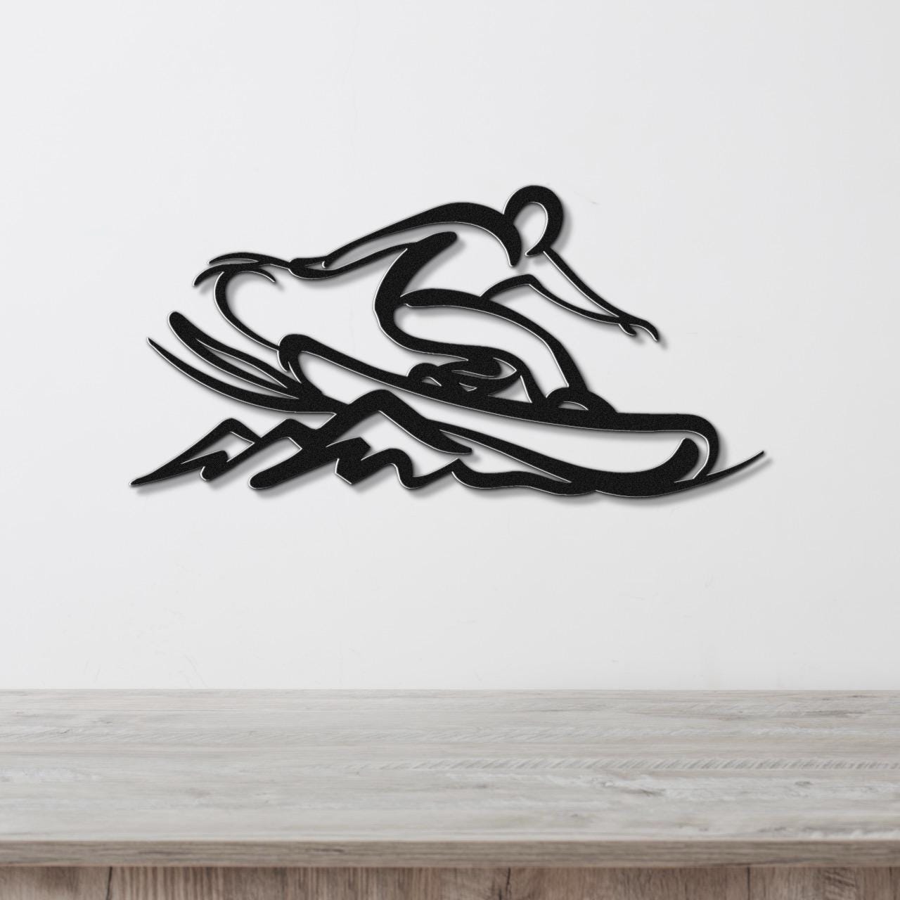 Black metal wall art silhouette of a snowboarder in motion, mounted on a white wall above a light wood surface.