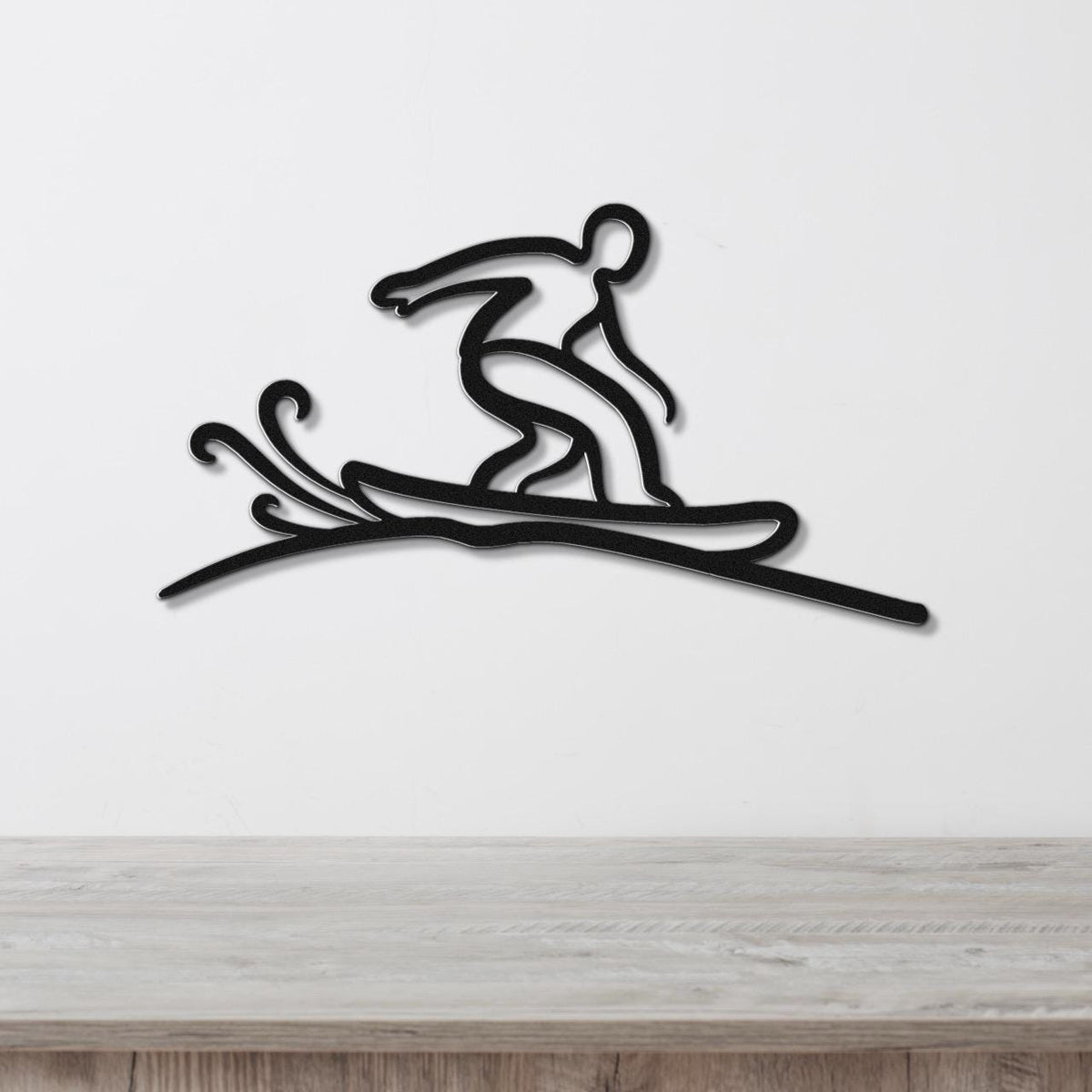 Black metal wall art silhouette of a snowboarder in motion, with dynamic cutout lines for snow spray, mounted on a white wall above a wooden surface.