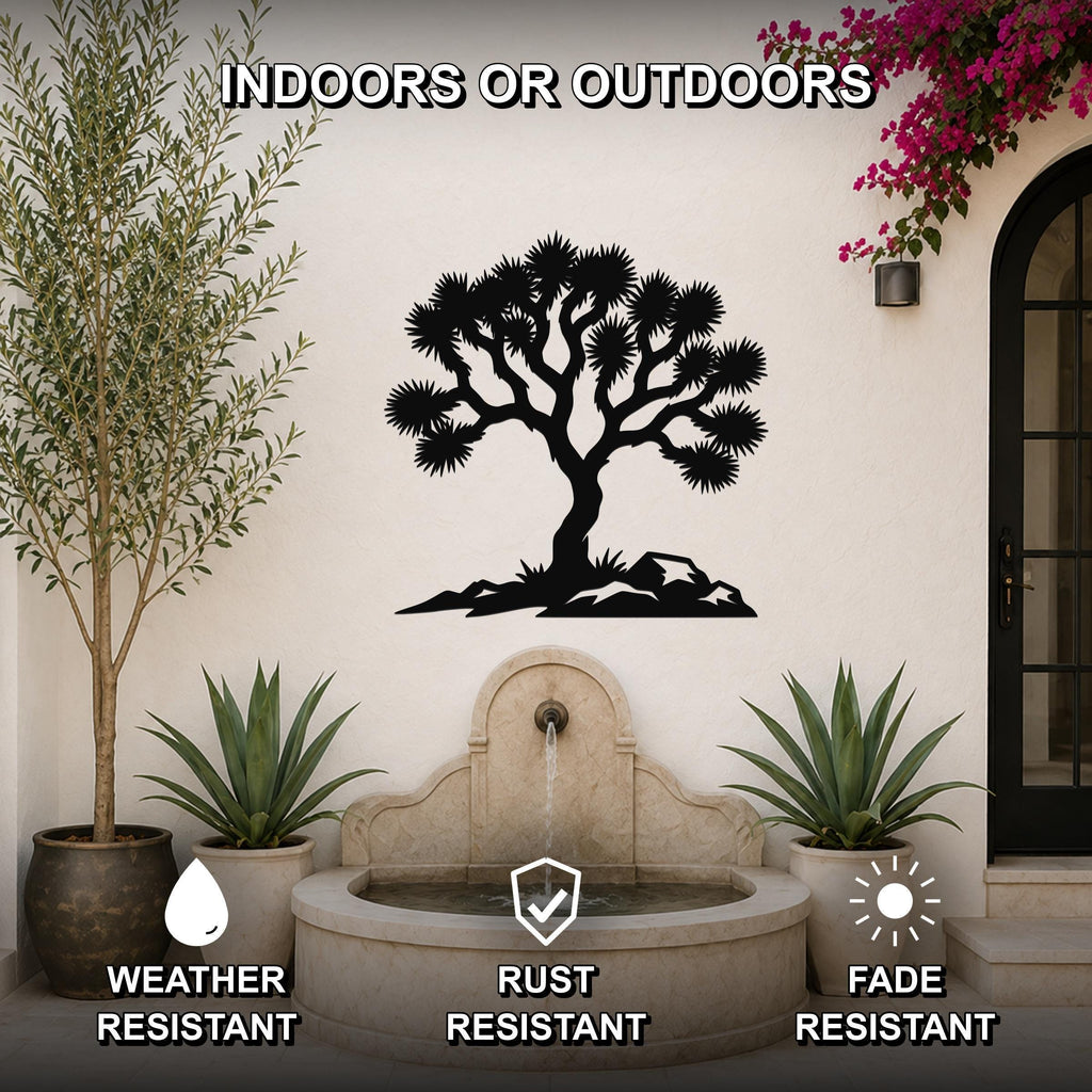 Black metal wall art featuring a Joshua tree silhouette with spiky branches and rocky base, mounted on an outdoor wall above a stone fountain in a patio setting.